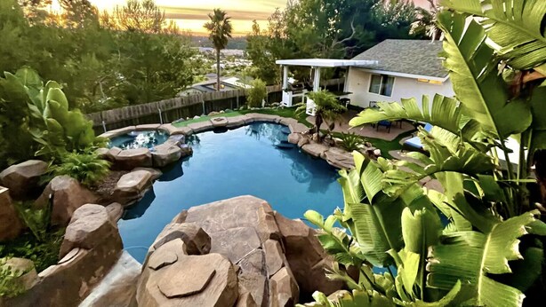 A backyard with a swimming pool surrounded by rocks and tropical plants. - Ocean View Poolside Retreat
 (Oceanside)
