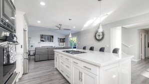 A modern kitchen with white cabinetry, a central island, and a dining area with chairs. - Ocean View Poolside Retreat
 (Oceanside)