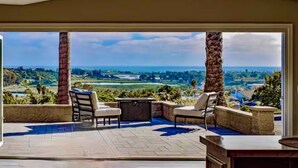 A patio with outdoor furniture, a view of a coastal landscape, and a clear sky. - Ocean View Poolside Retreat
 (Oceanside)