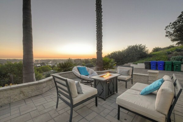 An outdoor patio with a fire feature, seating, and a view of the sunset.