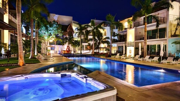 A hotel pool area with hot tubs, palm trees, and modern buildings.