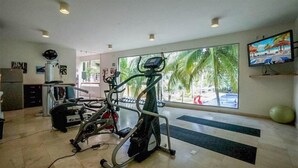 A gym with exercise equipment, a large window with a view of palm trees, and a TV mounted on the wall.