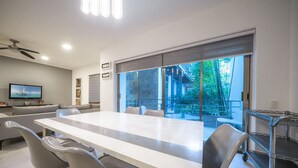 A modern dining area with a large table, chairs, a ceiling fan, and a television on the wall.