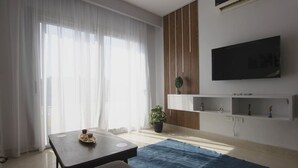 Una sala moderna con un ventanal grande, un televisor de pantalla plana en la pared, una mesa de centro, un sofá y una alfombra azul.