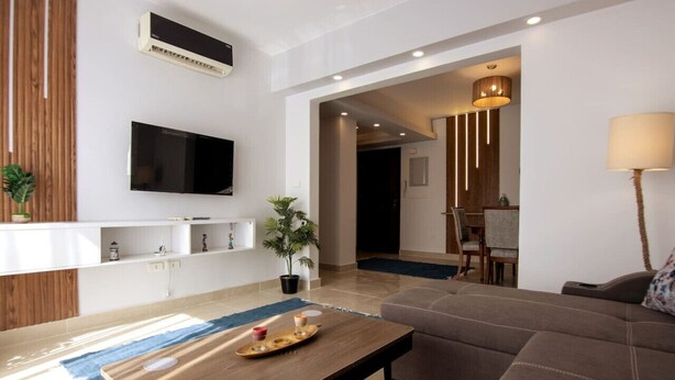 Una sala moderna con un sofá, una mesa de centro, un televisor y un comedor al fondo.