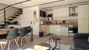 A modern kitchen with a dining area, a staircase, and a living room with a sofa and a coffee table.
