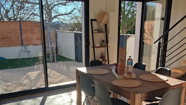 A modern dining area with a large table and chairs, a staircase, and a view of the outdoors.