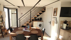 A modern kitchen with a built-in washing machine, a dining area with a wooden table and chairs, and a staircase leading to an upper level.