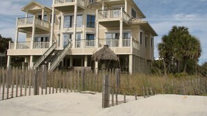 A multi-story beachfront property with balconies, a thatched roof structure, and a sandy beach in the foreground. - Plantation at St George Island Fl.. Beautiful beach view from all bedrooms . (Saint George Island)