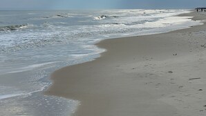 A beach with waves, a cloudy sky, and a few people in the distance. - Plantation at St George Island Fl.. Beautiful beach view from all bedrooms . (Saint George Island)