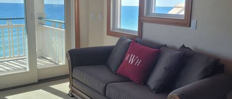 Una habitación con un sofá marrón oscuro, un cojín rojo con la inscripción 'RWH' y vistas al océano a través de amplios ventanales.