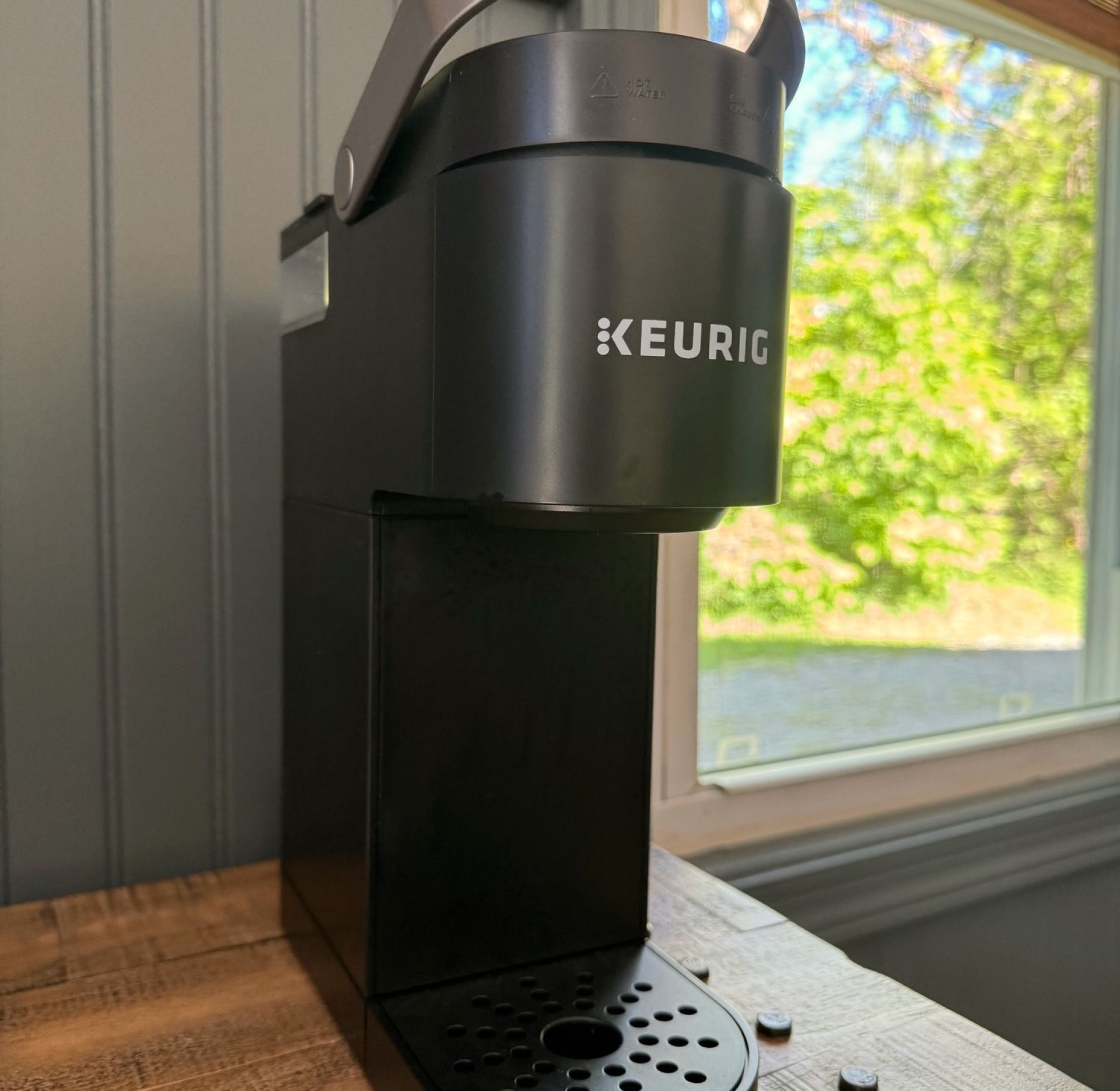 A black Keurig coffee maker on a wooden surface near a window.