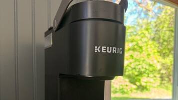 A black Keurig coffee maker on a wooden surface near a window.