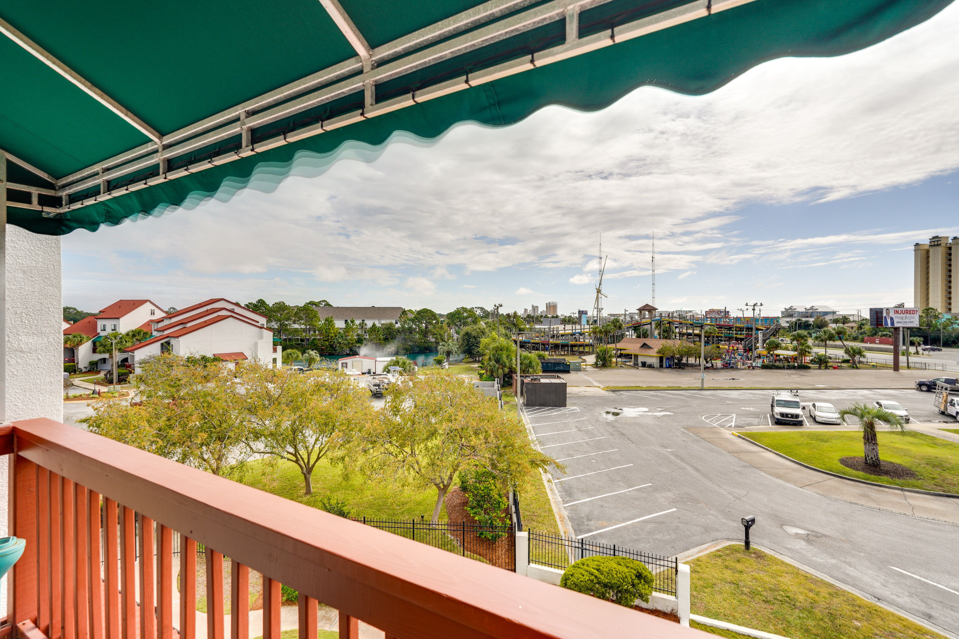 Une vue depuis un balcon donnant sur un parking et sur le paysage urbain, avec ses bâtiments et ses arbres.