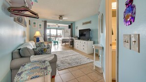 A living room with a sofa, TV, and decorative items. There is a dining area with chairs and a table. The room has light blue walls and a ceiling fan. - Panama City Beach Getaway - Walk to Beaches! (Panama City)