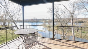 Un espacio al aire libre cubierto con una mesa y sillas, con vistas a un lago y árboles.