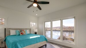Un dormitorio con una cama grande, un ventilador de techo y vistas a un lago a través de amplias ventanas.