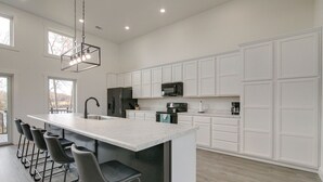Una cocina moderna con una isla grande, taburetes de bar, armarios blancos y una lámpara colgante.