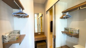 Un couloir étroit au plancher en bois, avec un miroir et deux étagères en bois où sont suspendus des vêtements et rangés des articles de toilette.