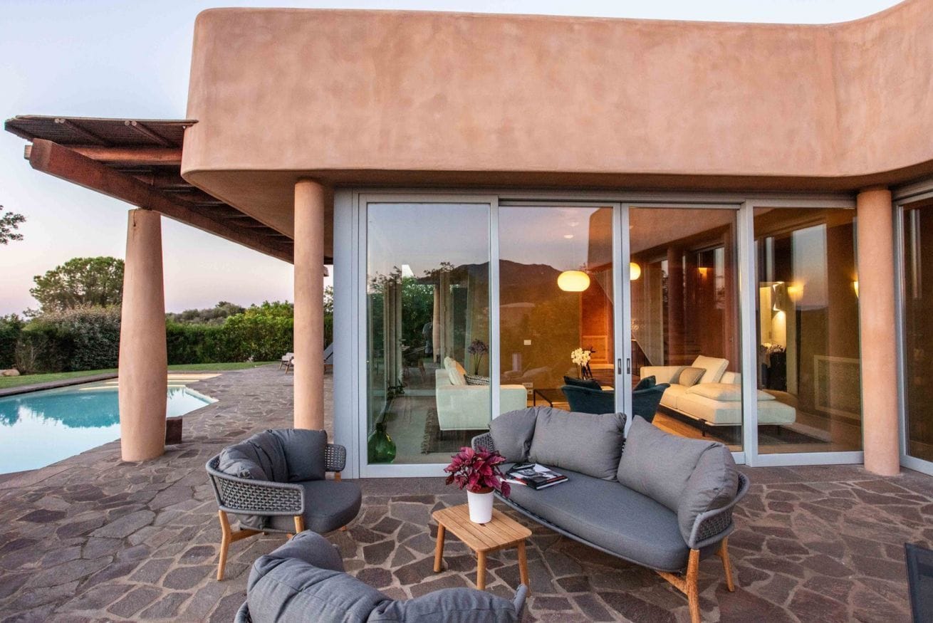 Una zona living esterna moderna con piscina, pavimento in pietra e un'ampia porta scorrevole in vetro che dà accesso a un ambiente interno luminoso.
