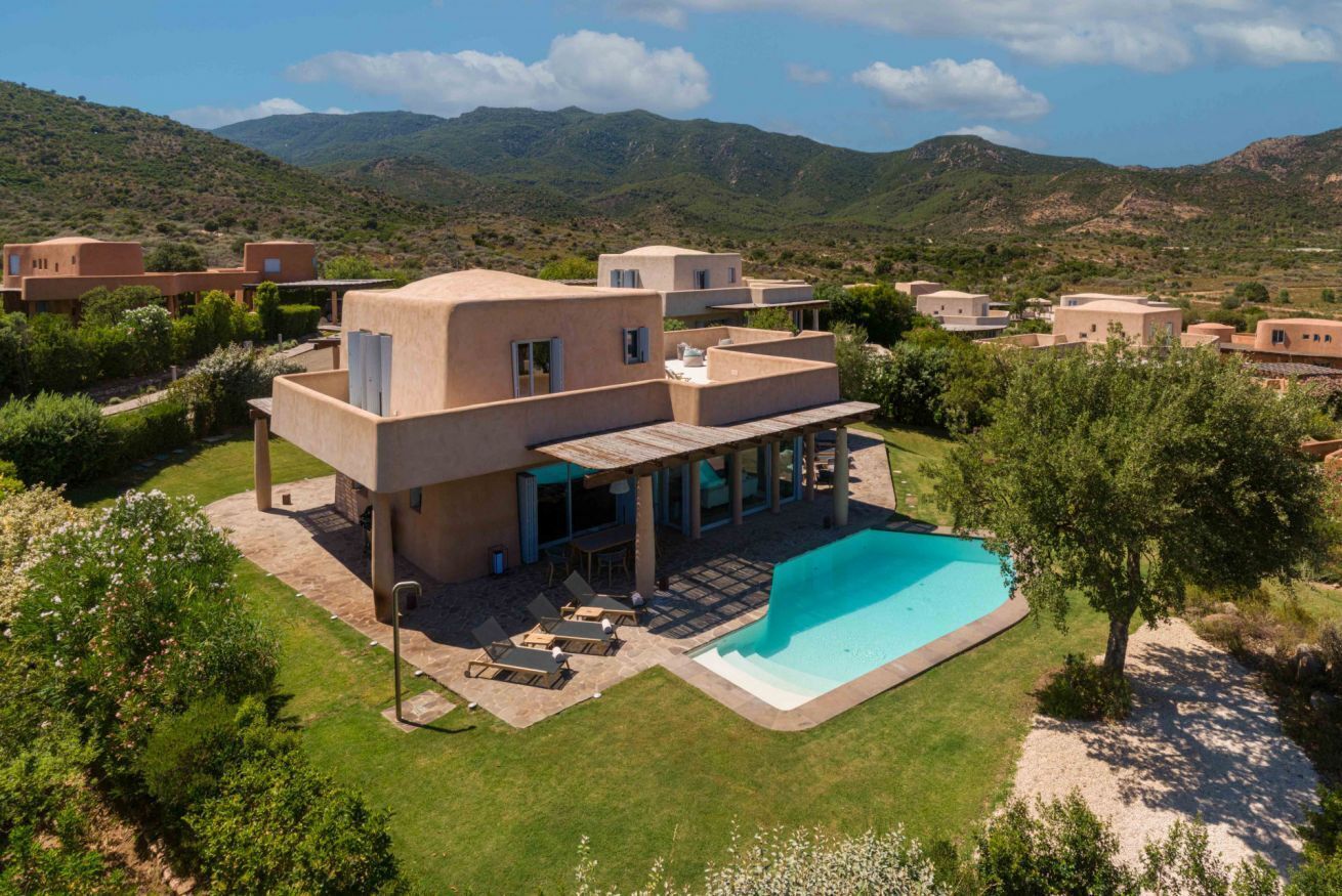 A modern villa with a swimming pool, surrounded by lush greenery and hills.