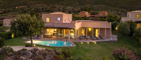 A modern villa with a swimming pool, surrounded by lush greenery and hills.