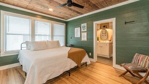 Ein Schlafzimmer mit Bett, Stuhl, Deckenventilator und einem Bad mit Spiegel und Waschbecken.