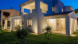 A modern two-story house with a flat roof, large windows, and a well-lit exterior. - Residenza L'Alzoni (San Teodoro)