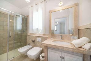 A modern bathroom with a glass shower enclosure, a bidet, a sink with a large mirror, and a towel rack.