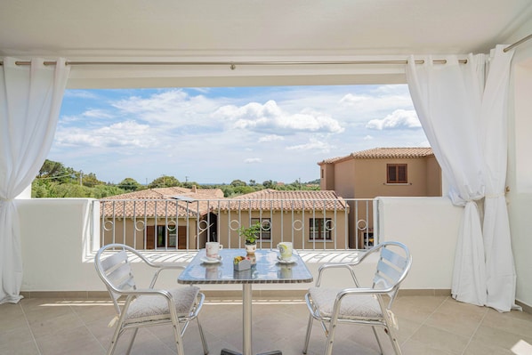 A balcony with a table and chairs, overlooking a residential area with houses and greenery.