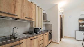 A modern kitchen with wooden cabinets, a stainless steel sink, a microwave, and a gas stove. - Residenza L'Alzoni (San Teodoro)