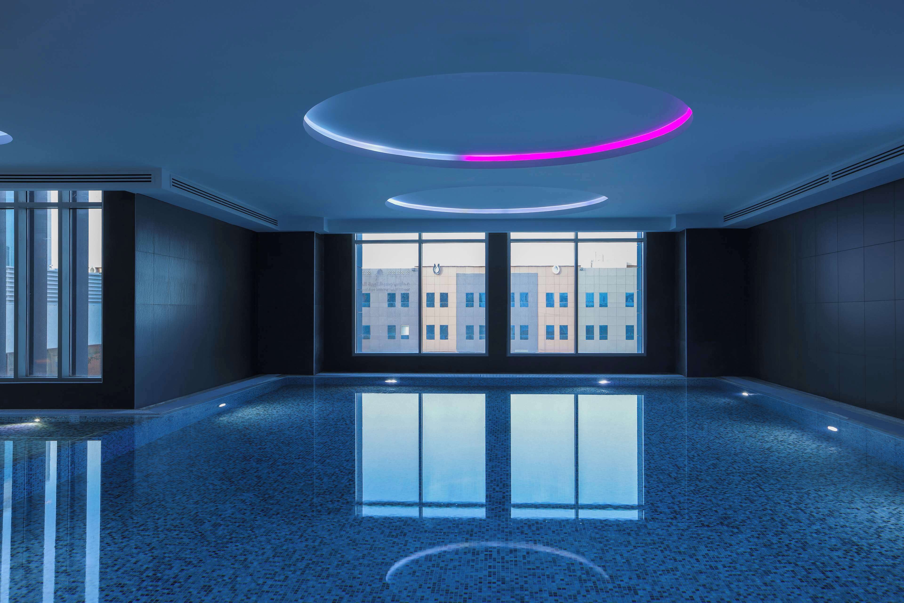 A spacious indoor area with a reflective floor, large windows, and modern circular ceiling lights.