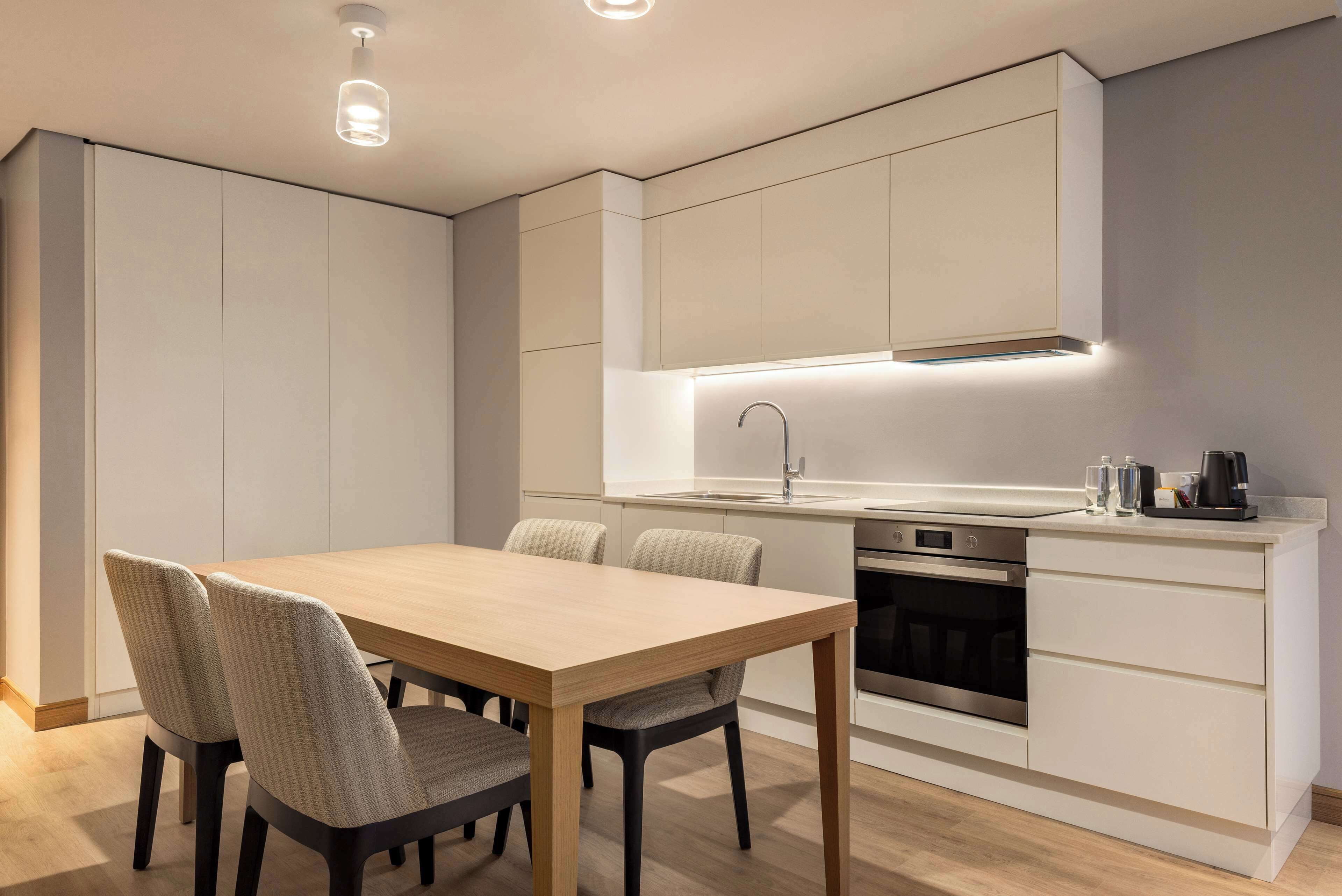 A modern kitchen with a wooden dining table, built-in cabinets, and a stainless steel oven.