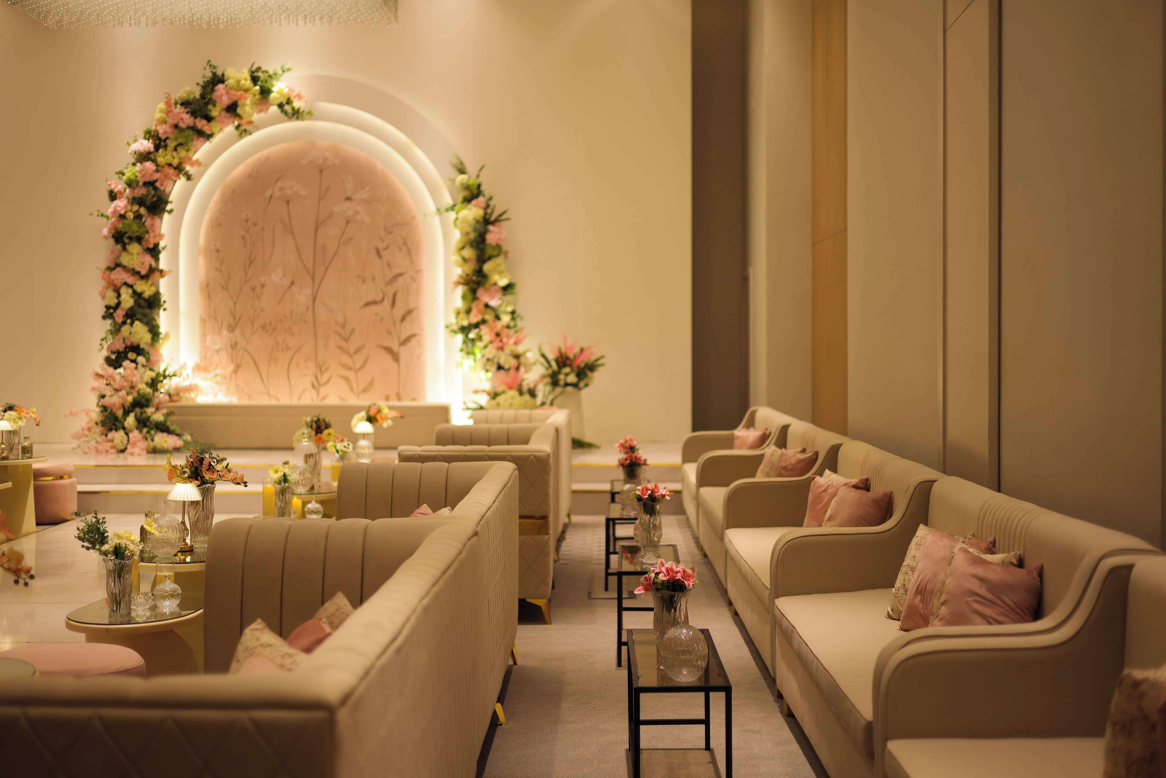 A modern lounge area with sofas and tables, decorated with floral arrangements and candles.