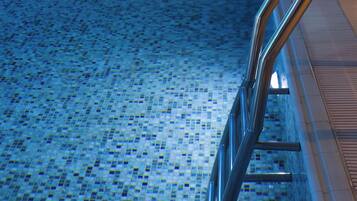 A swimming pool with a tiled floor and metal handrails.