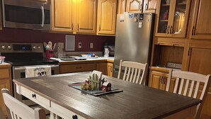 Una cocina con armarios de madera, un refrigerador de acero inoxidable, un microondas y una mesa de comedor con sillas.