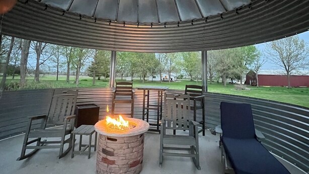 Un espacio de estar al aire libre techado con un brasero, sillas y una tumbona.
