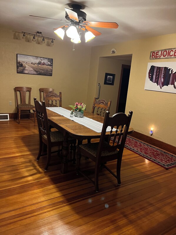 Comedor con mesa de madera, sillas, ventilador de techo y lámpara fijada a la pared.