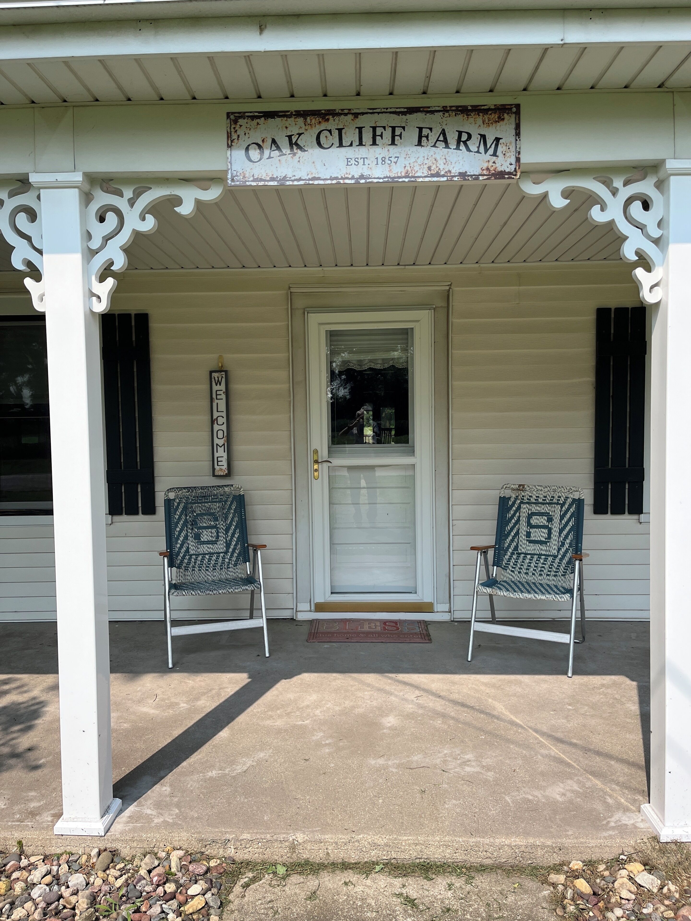 Une véranda avec une enseigne indiquant « Oak Cliff Farm » et deux chaises.
