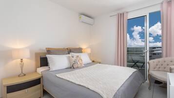Un dormitorio con cama, mesita de noche, lámpara y vista al cielo a través de la ventana.