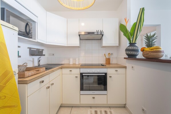 A modern kitchen with white cabinetry, a built-in oven, and a microwave. There is a wooden countertop and a vase with a plant and fruit on the side.