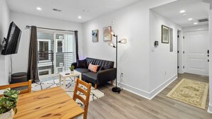 Ein modernes Wohnzimmer mit einer schwarzen Ledersofa, einem Holzesstisch und einem an der Wand befestigten Fernseher.