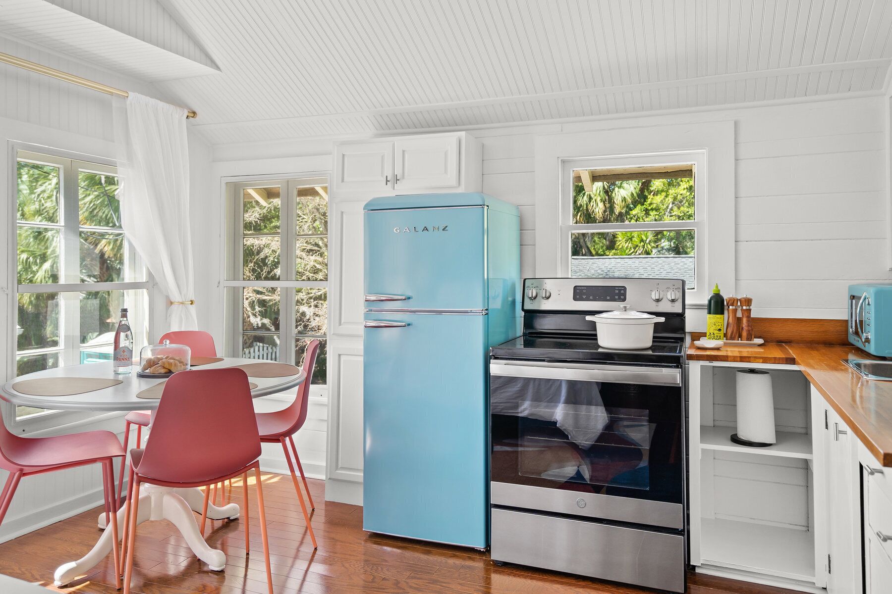 Een keuken met een blauwe koelkast, een fornuis en een eethoek met roze stoelen.
