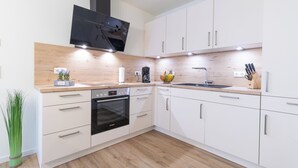 A modern kitchen with white cabinets, a Bosch oven, a black range hood, and a wooden countertop.