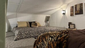 A bedroom with a sloped ceiling, a bed with a leopard print cover, a brown throw blanket, and a wall-mounted light fixture. - The Pecan at Hamilton Cove ~ Cabin Twenty ~ Lakefront ~ Pet Friendly (Royal)