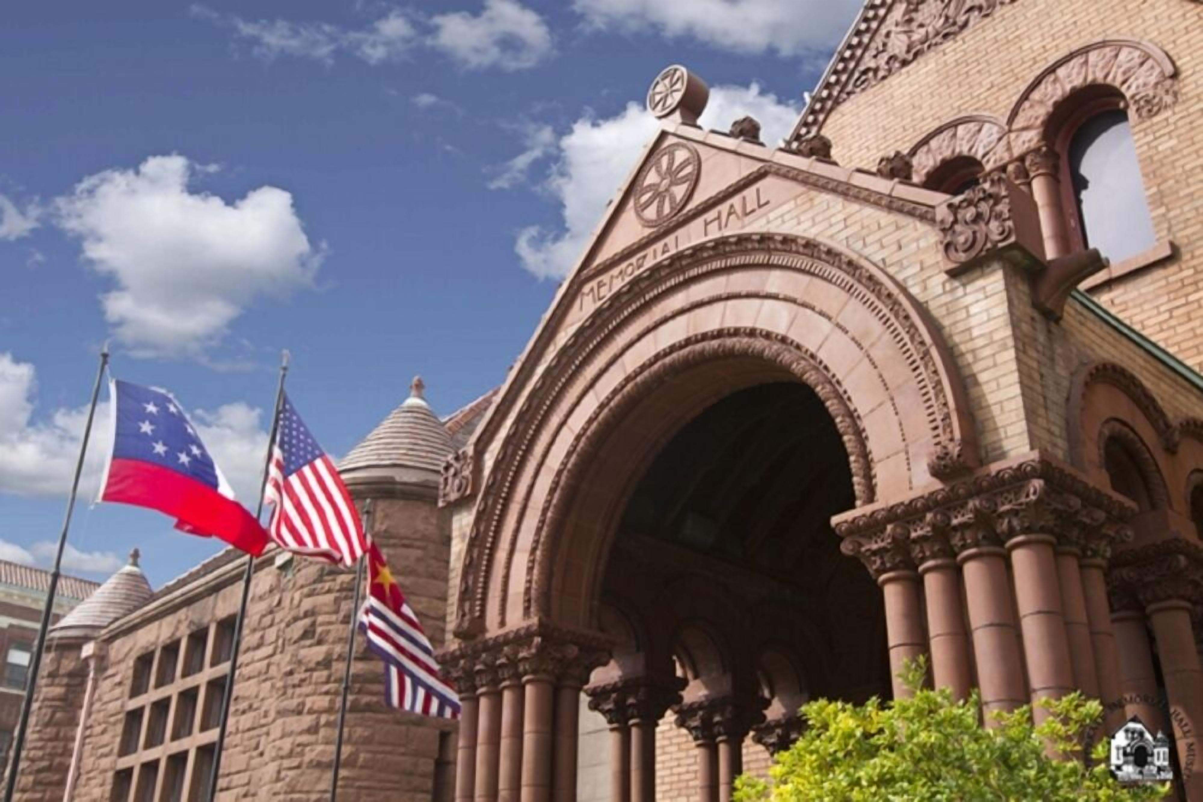 Un bâtiment historique doté d’une arche imposante et d’une tour horloge, sur laquelle flottent le drapeau américain et le drapeau de l’État du Texas.