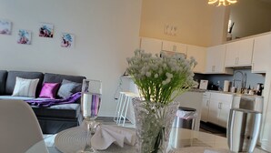Una sala moderna con un sofá, una mesa de comedor con sillas, un florero con flores y una cocina al fondo.