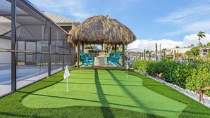 A well-maintained outdoor area with artificial grass, a thatched-roof structure, and seating.