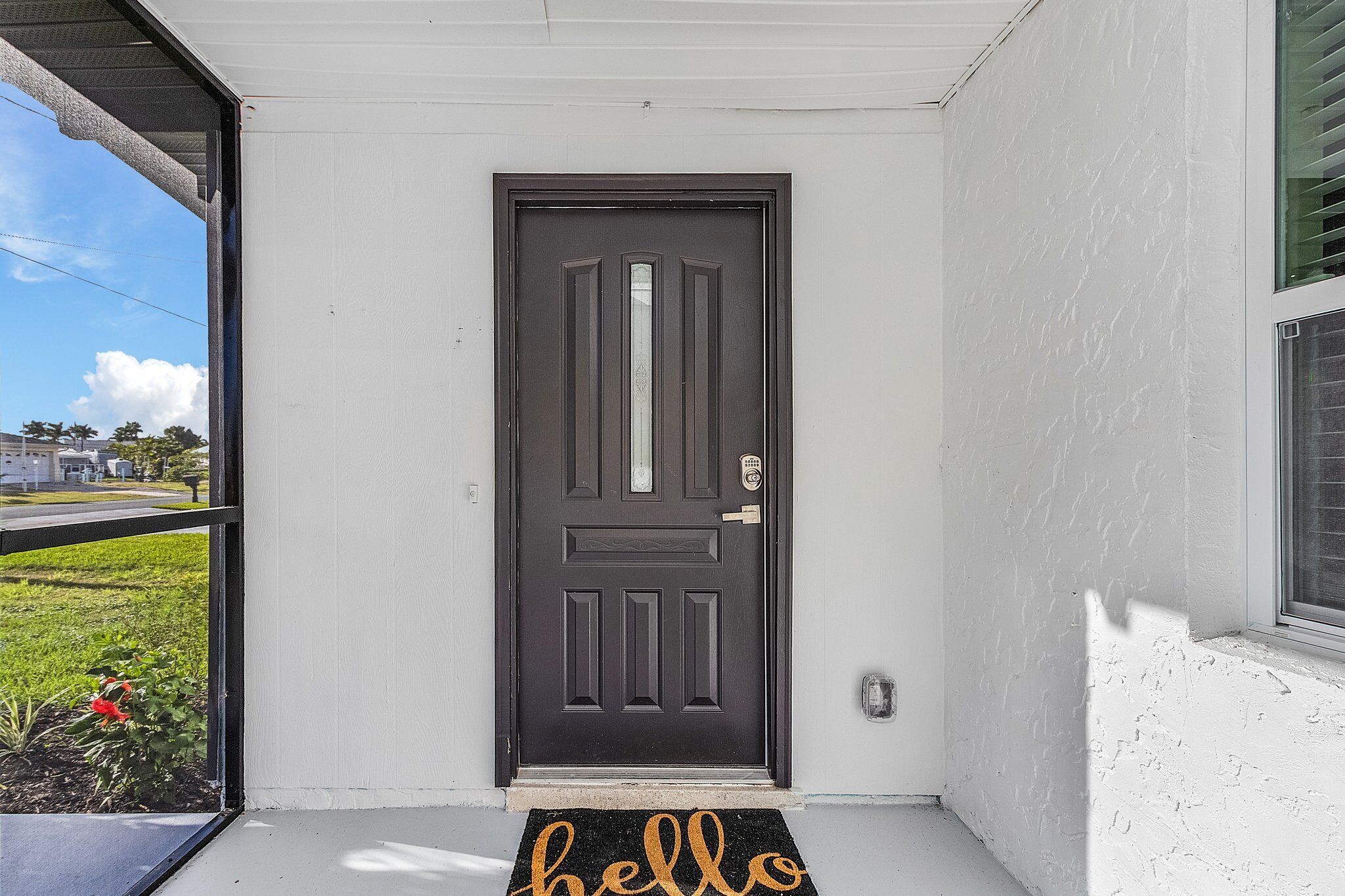 A black door with a doormat that reads "hello" on a porch with white walls.