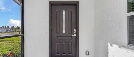 A black door with a doormat that reads "hello" on a porch with white walls.